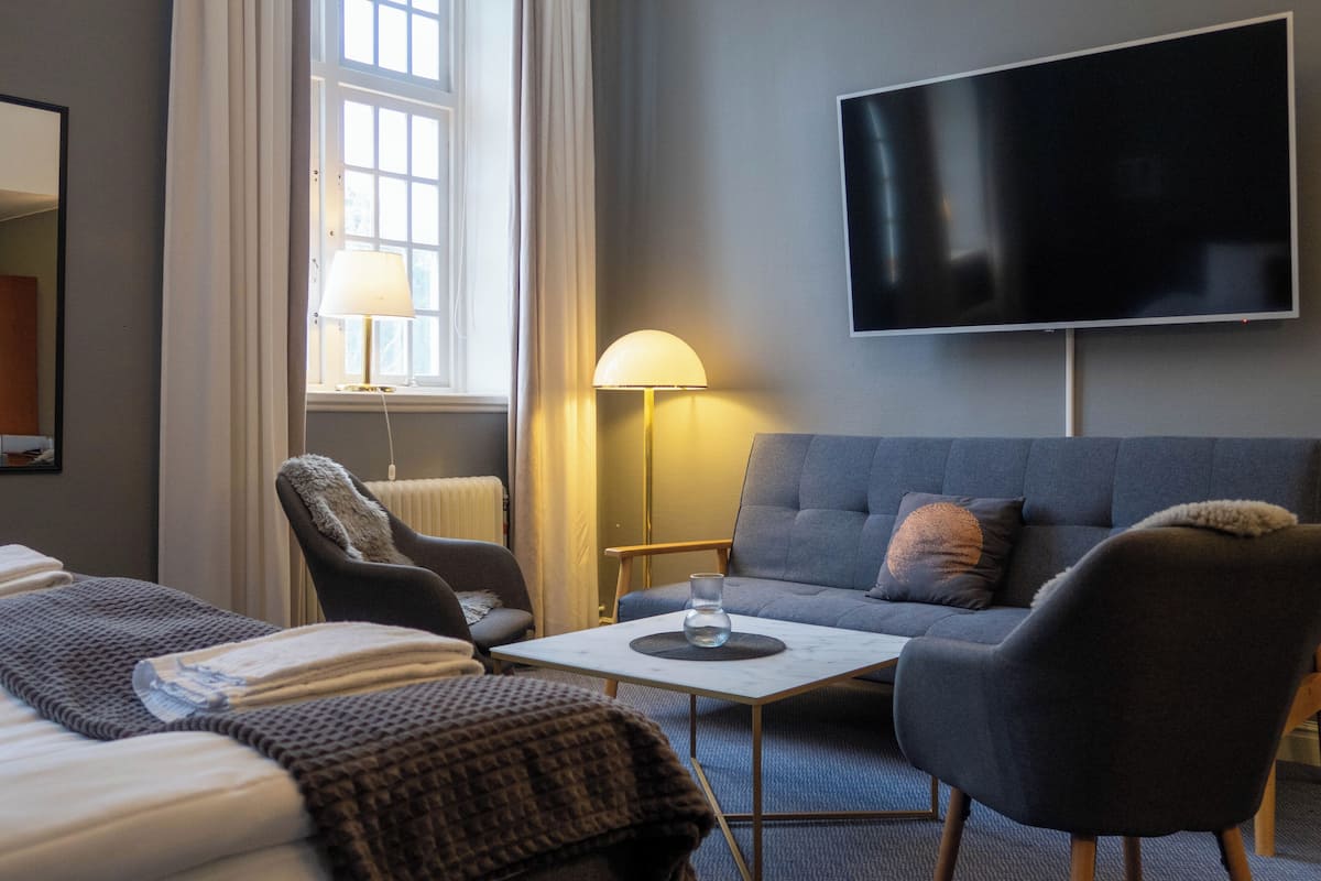 A hotel room with a sofa, armchair, and a flat-screen TV mounted on the wall.