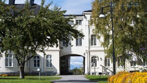 A building with a central archway, surrounded by greenery and a pathway leading to it. - Furunäset Hotell och Konferens (Pitea)