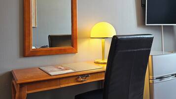 Habitación de hotel con escritorio de madera, una silla de cuero negro, espejo, lámpara y televisor.