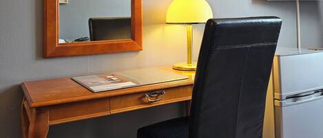 A hotel room with a wooden desk, a black leather chair, a mirror, a lamp, and a television.