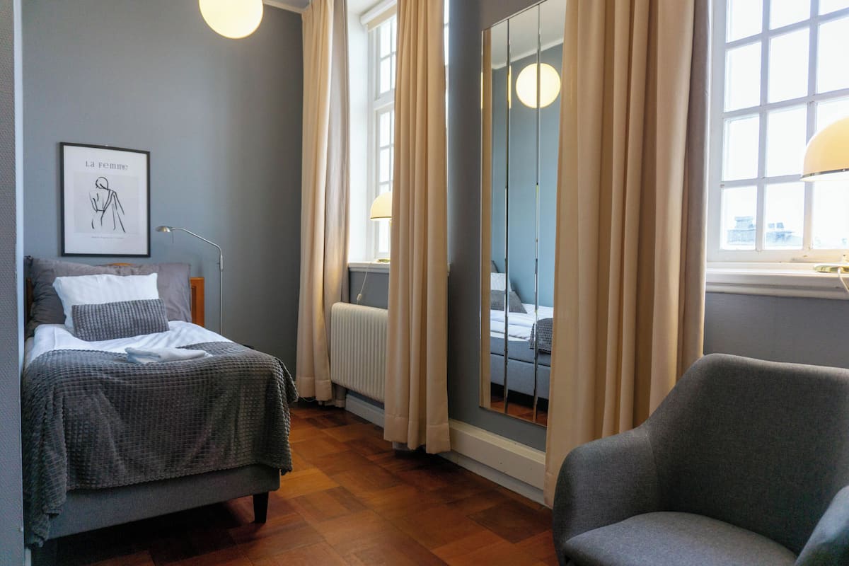 A bedroom with a bed, a chair, a radiator, a window with curtains, and a framed picture on the wall.