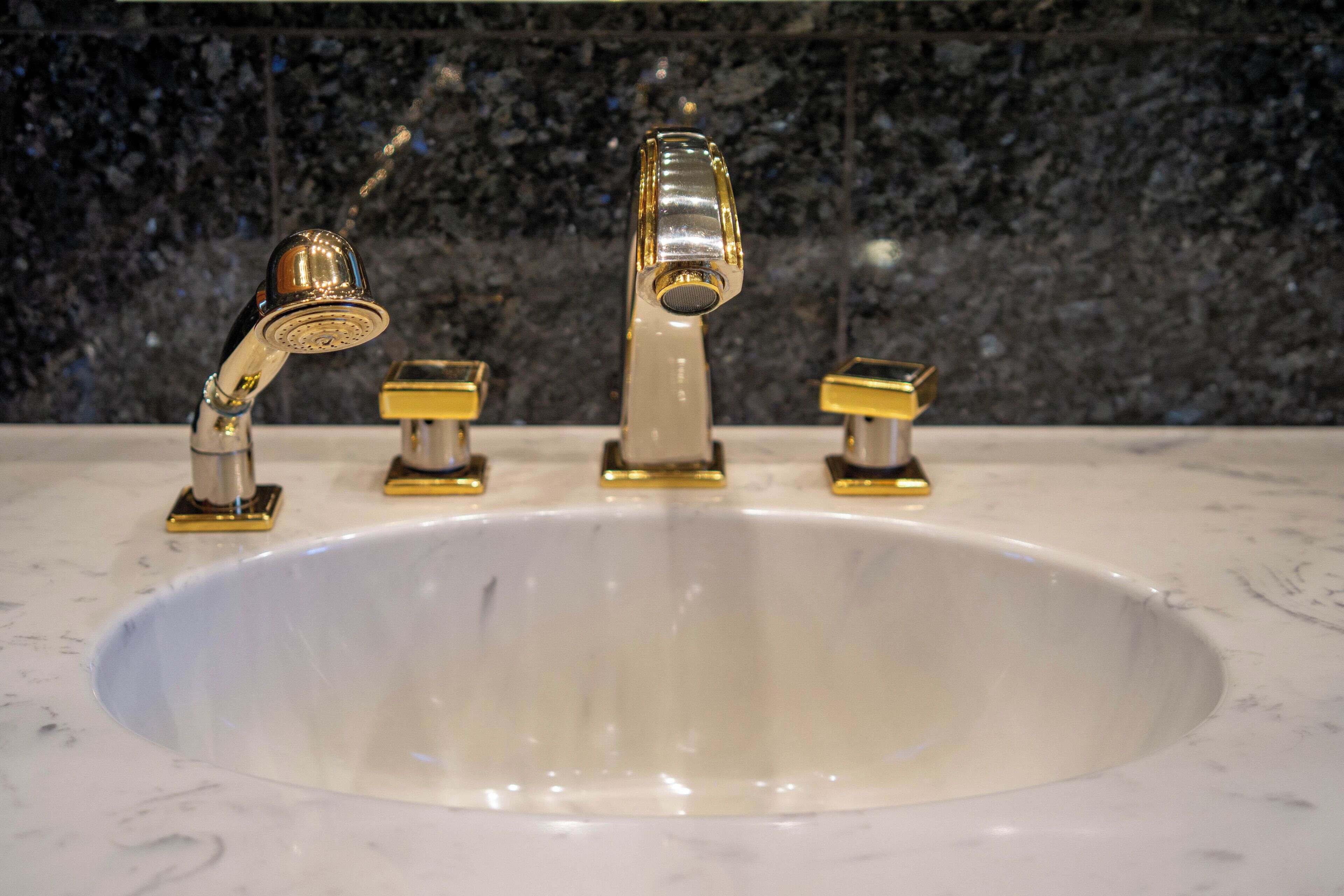 Un lavabo de salle de bain avec un plan de toilette en marbre et trois robinets dorés.