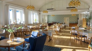 A spacious dining area with multiple tables and chairs, large windows allowing natural light, and a high ceiling with decorative lighting fixtures. - Furunäset Hotell och Konferens (Pitea)