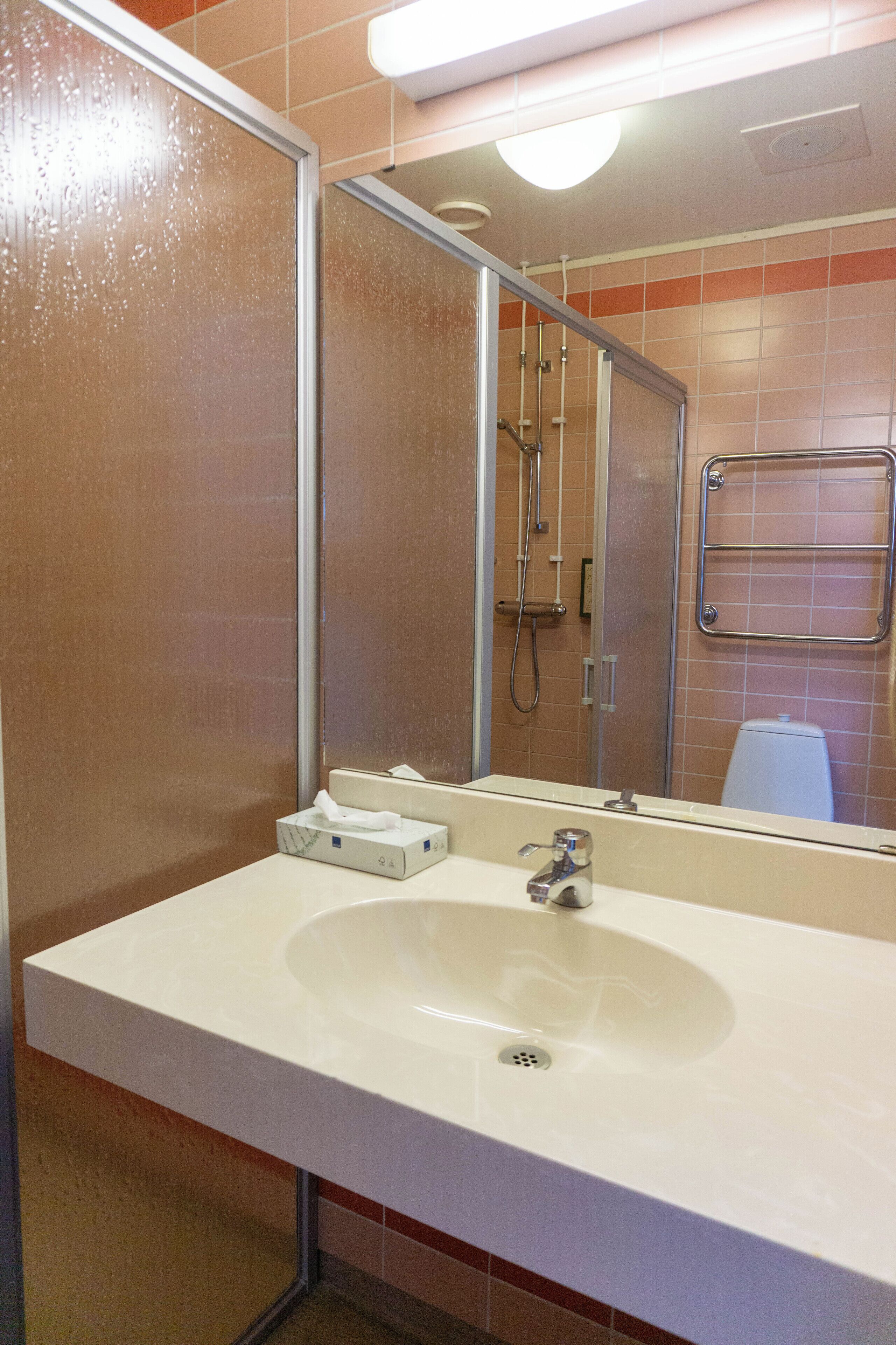 A bathroom with a white sink, a mirror, a towel dispenser, and a shower area.