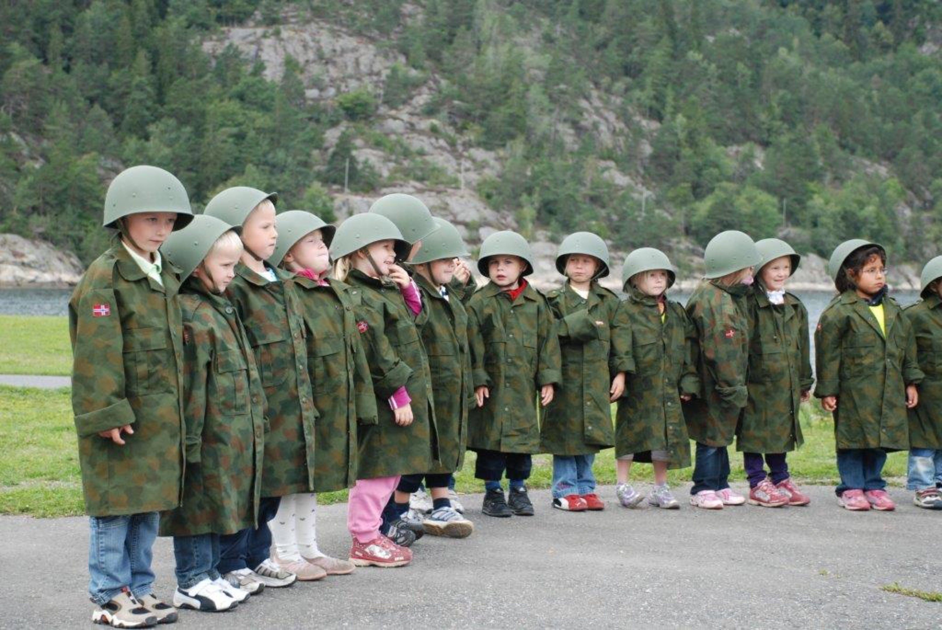 A group of children in military-style uniforms and helmets standing in a line outdoors.