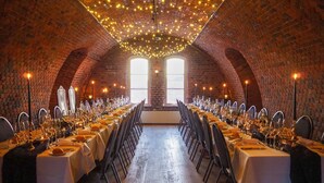 A long dining table set in a brick-walled room with string lights overhead. - Oscarsborg Castle Hotel & Resort (Frogn)