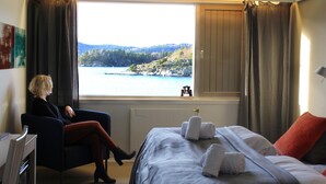 A room with a bed, a chair, a window with a view of a lake and hills, and a radiator. - Oscarsborg Castle Hotel & Resort (Frogn)