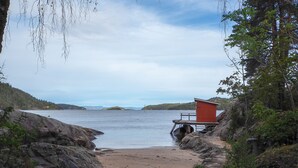 A beach with a wooden walkway leading to a red building, surrounded by rocky terrain and trees. - Oscarsborg Castle Hotel & Resort (Frogn)