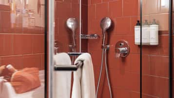 A bathroom with a glass shower enclosure, a towel rack, and toiletries on the wall.