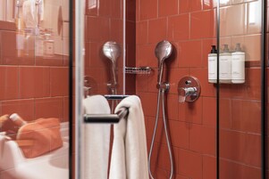 A bathroom with a glass shower enclosure, a towel rack, and toiletries on the wall.