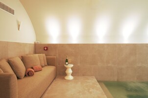 Un cuarto de spa con un sofá color beige, una mesita blanca y una botella de vino, además de un calentador fijado a la pared.