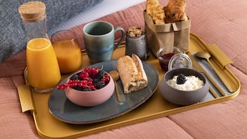 Bandeja de desayuno con un croissant, bayas, yogur y jugo sobre una cama con una manta.