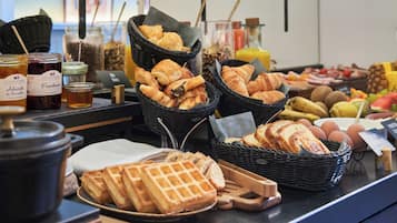 Een ontbijtbuffet met manden croissants, wafels en verschillende soorten jam.