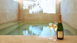 A pool area with a projection screen displaying a crowd, a bottle of champagne, and two glasses on a table. - Dadou Paris (Paris)