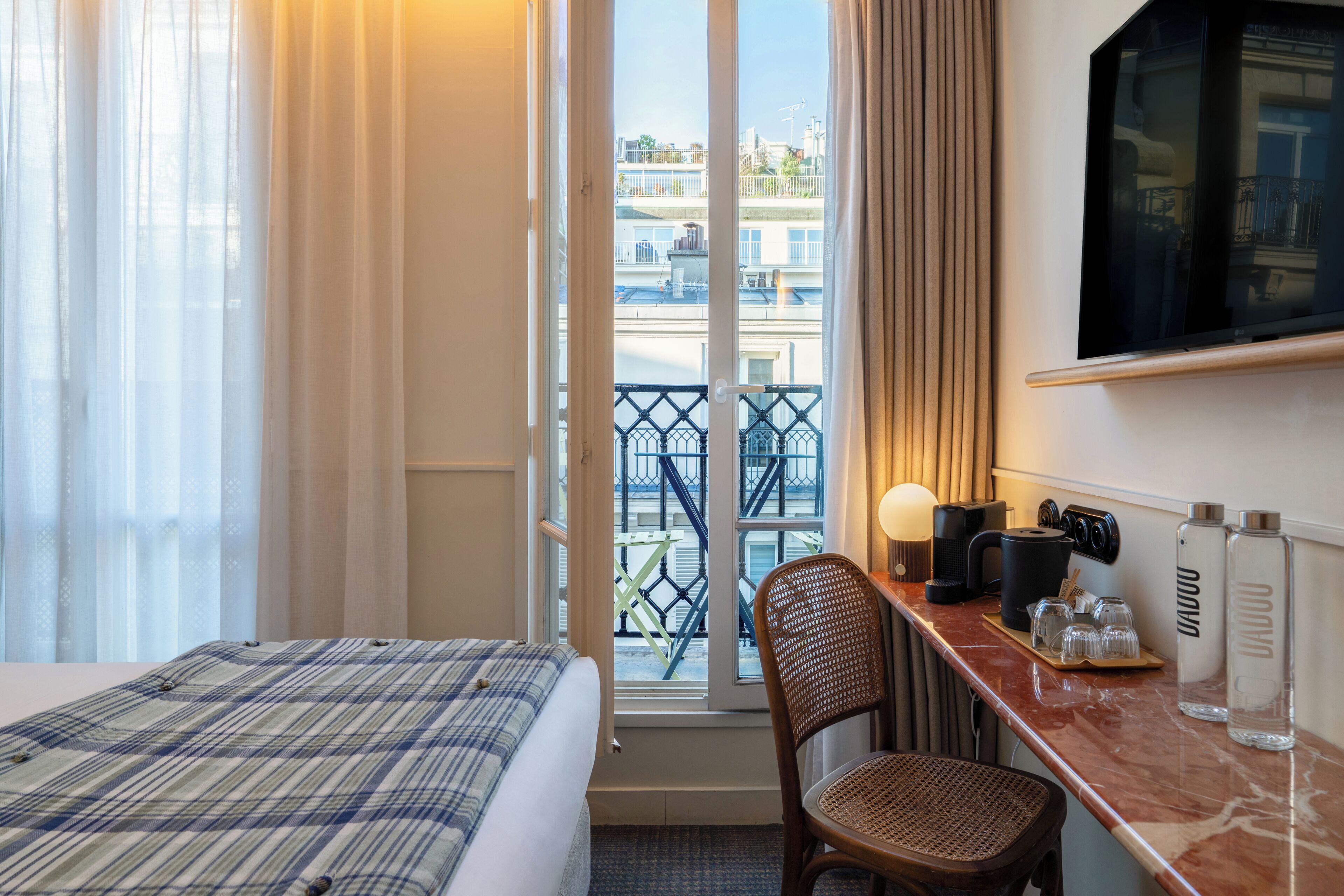A hotel room with a bed, a desk with a chair, a television, and a view of the city through the window.