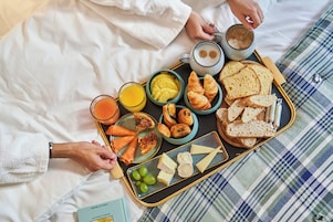 Un vassoio della colazione con croissant, formaggio, uva e una tazza di caffè su un letto con copriletto a quadri.