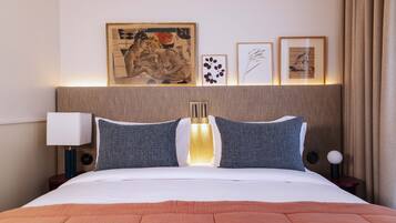 A neatly made bed with a white and orange bedspread, a headboard with a built-in light, and framed artwork on the wall.