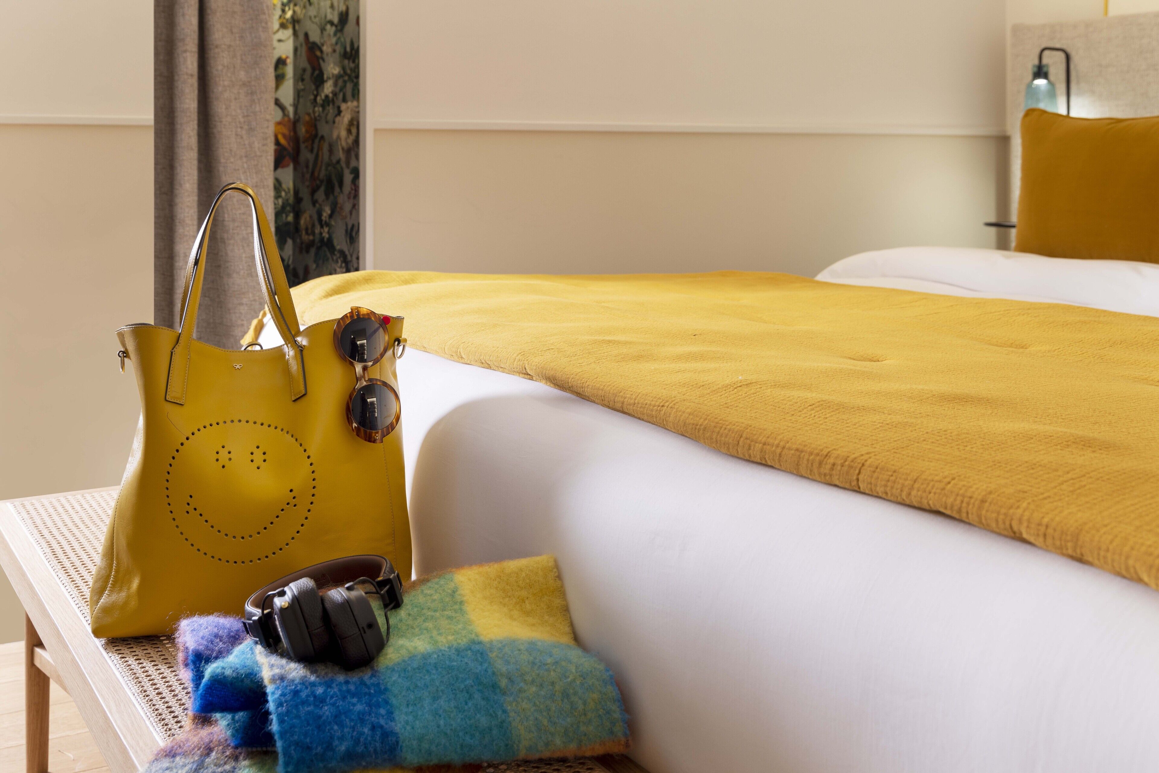 Un lit bien fait, avec une couverture jaune, un oreiller jaune et un sac à main jaune posé sur un banc en bois.