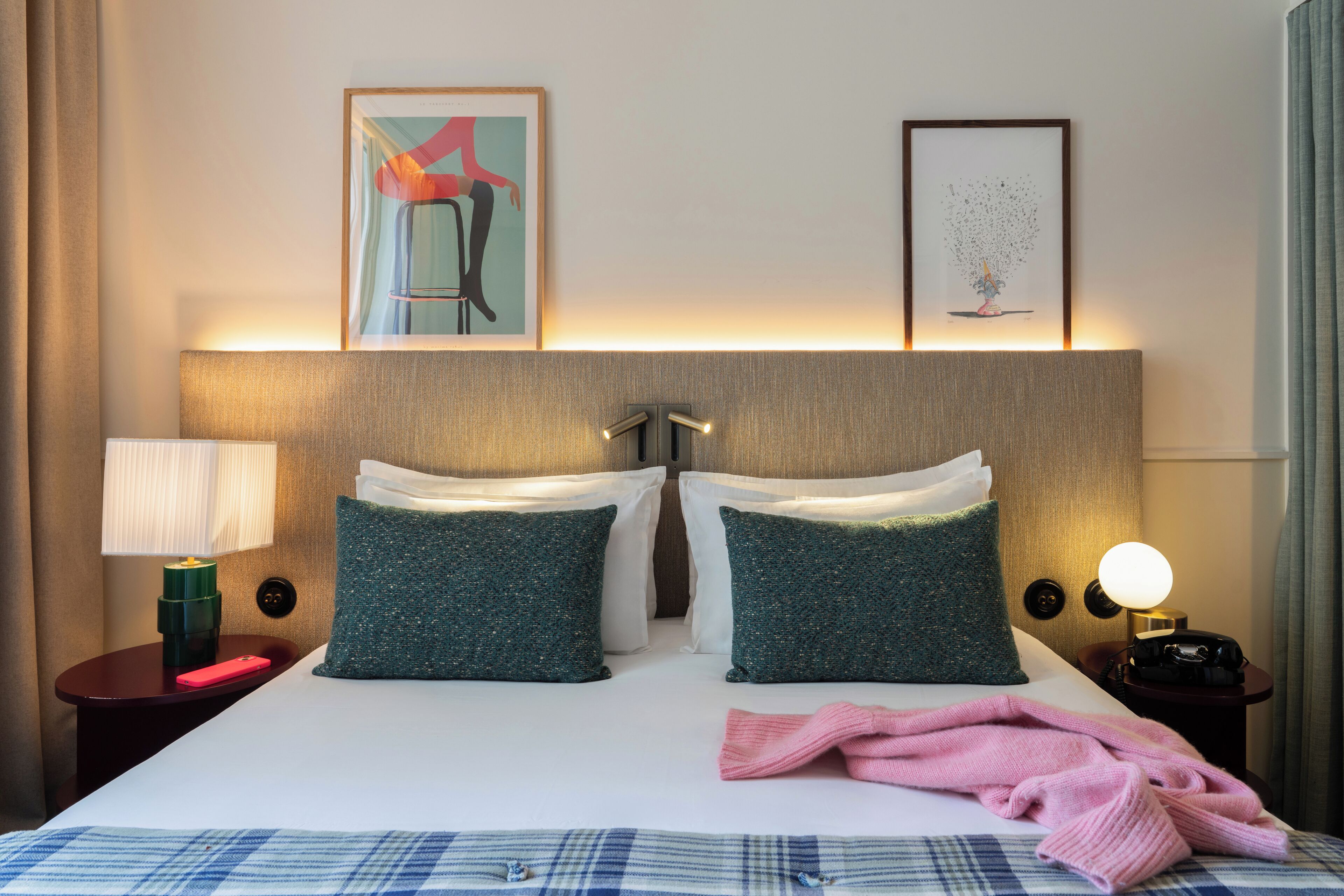 Habitación de hotel con cama, dos almohadas, una manta, lámpara, teléfono y una obra de arte en la pared.