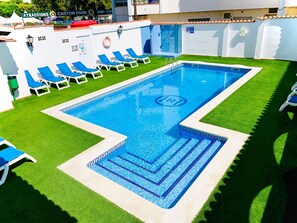 A swimming pool with blue tiles, surrounded by green artificial grass and white lounge chairs. - Hotel Comarruga Platja (El Vendrell)