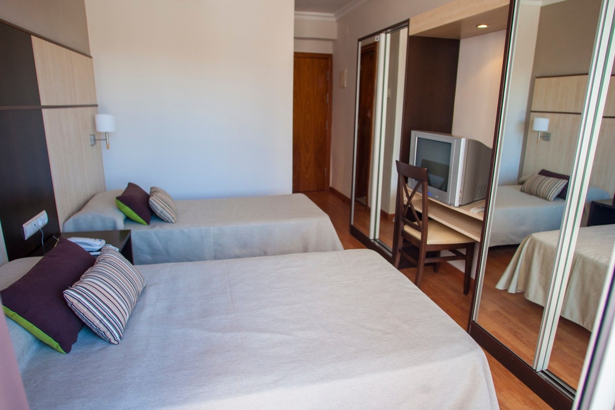 A hotel room with two beds, a desk, a television, and a mirror.