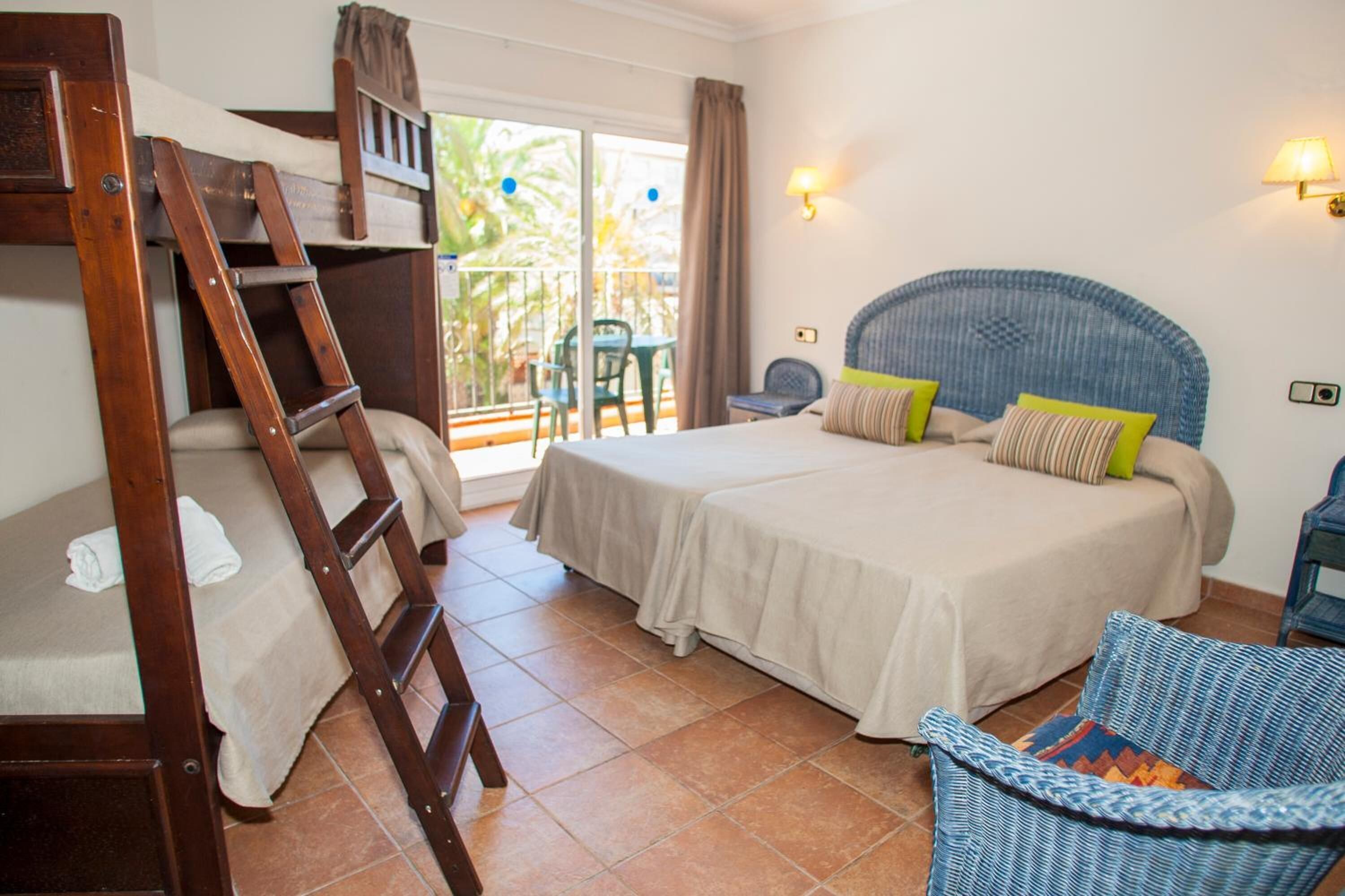 Un dormitorio con una cama litera, una cama doble, un balcón con sillas y una silla de mimbre.
