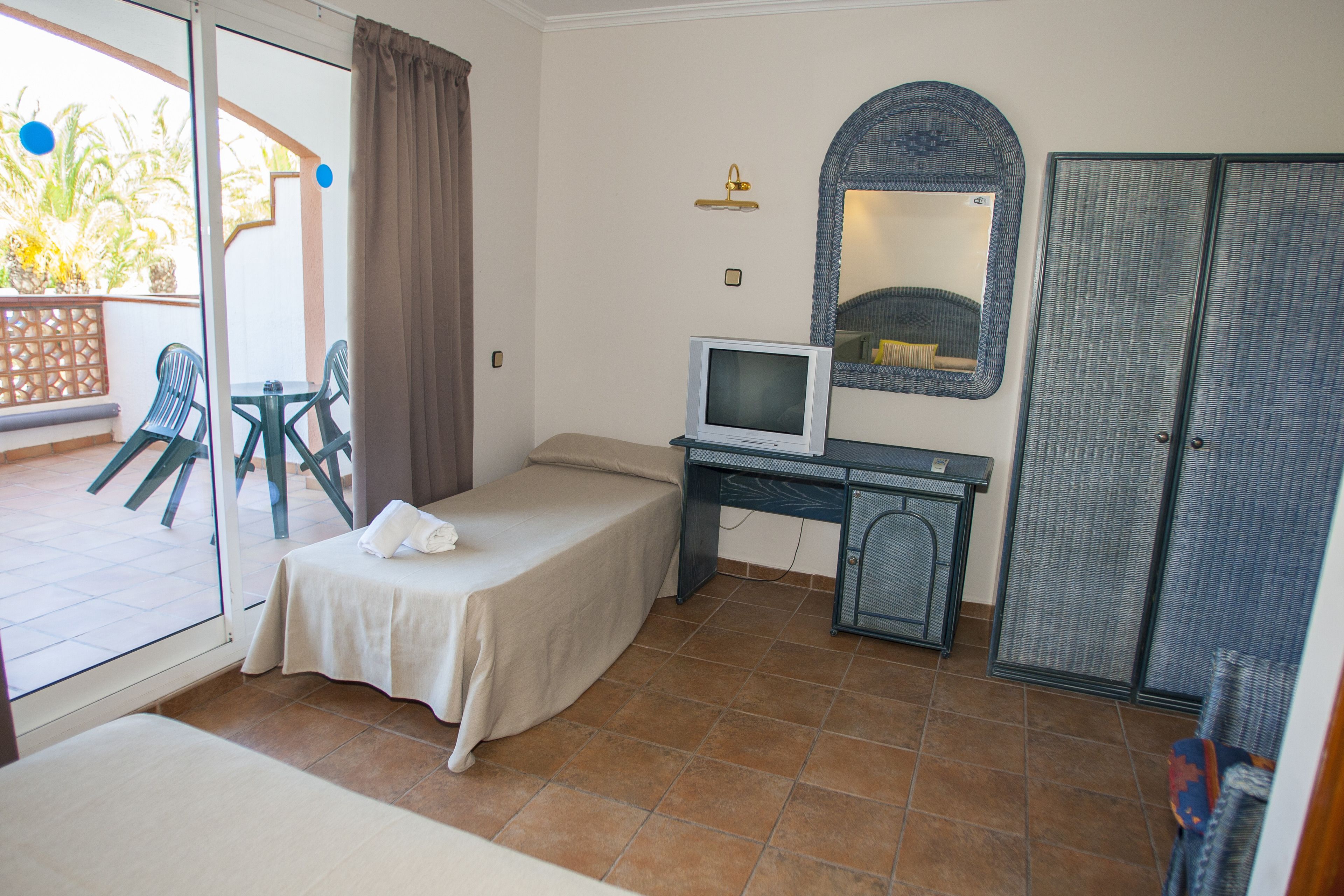 Una habitación de hotel con una cama, un escritorio con televisor, un armario y un balcón con sillas.