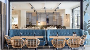 Un comedor moderno con una banca tapizada en azul, mesas de madera y sillas de mimbre.