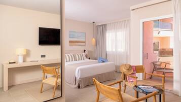 Habitación de hotel con cama, escritorio, silla, mesa pequeña, televisión y ventana con cortinas.