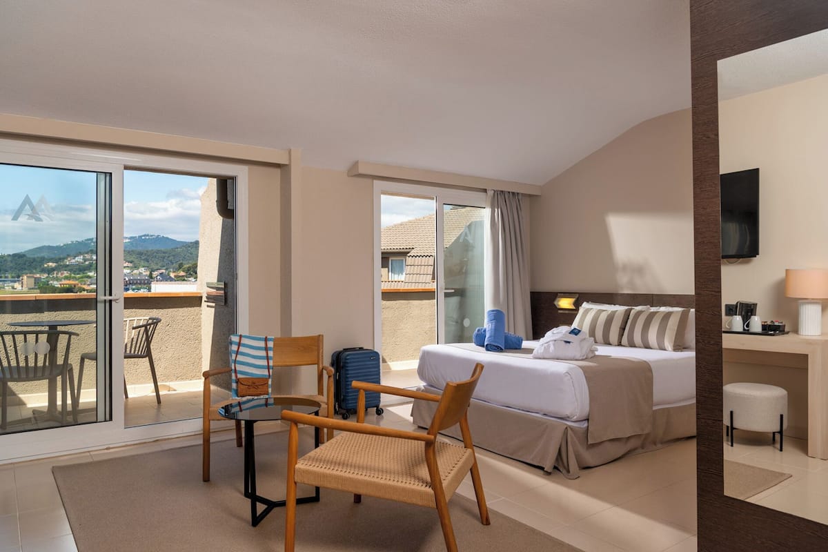 Habitación de hotel con cama, escritorio, silla, mesa y balcón con vistas al paisaje.