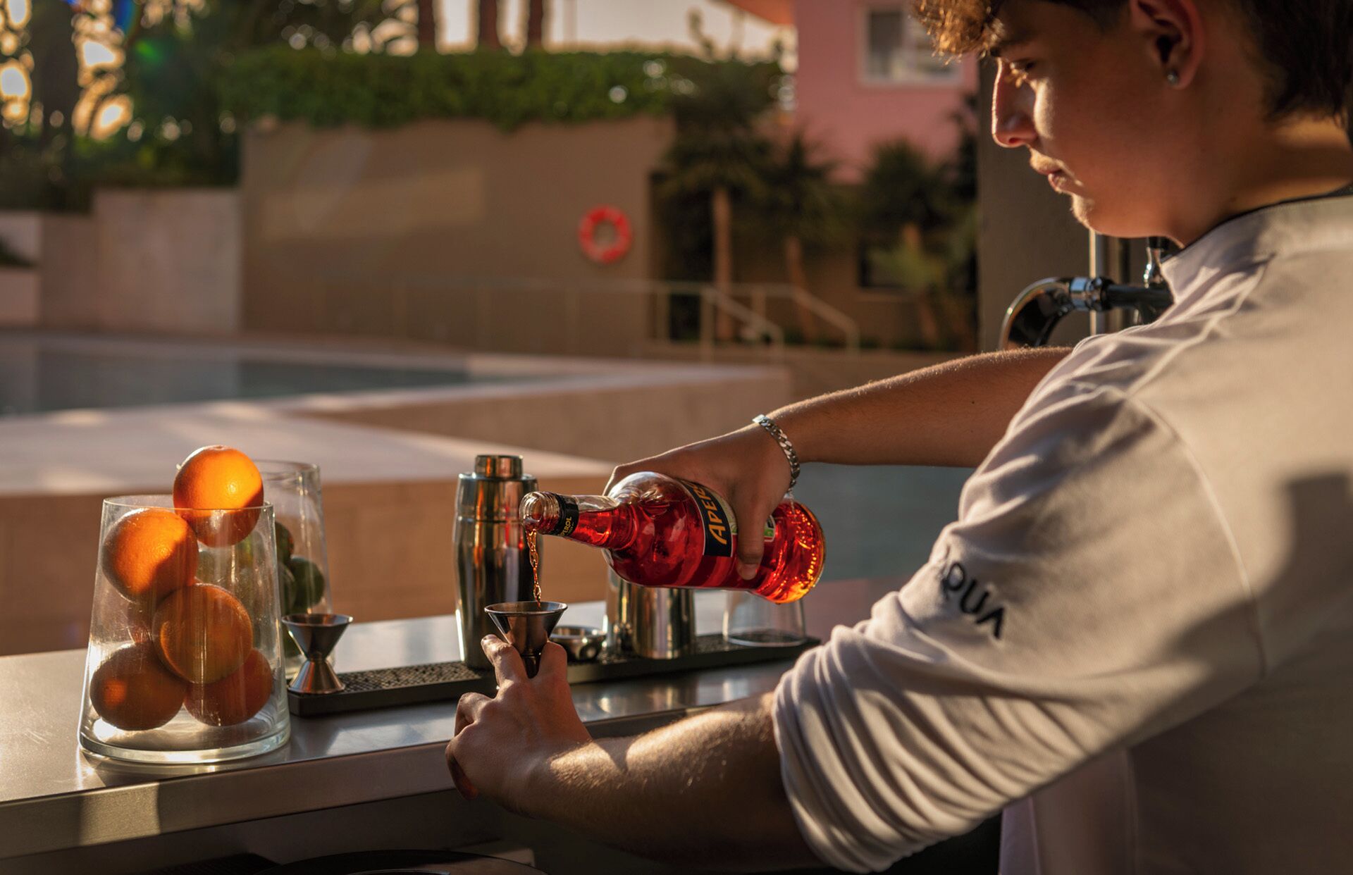 Una persona vertiendo un líquido rojo desde una botella a una coctelera sobre una barra.
