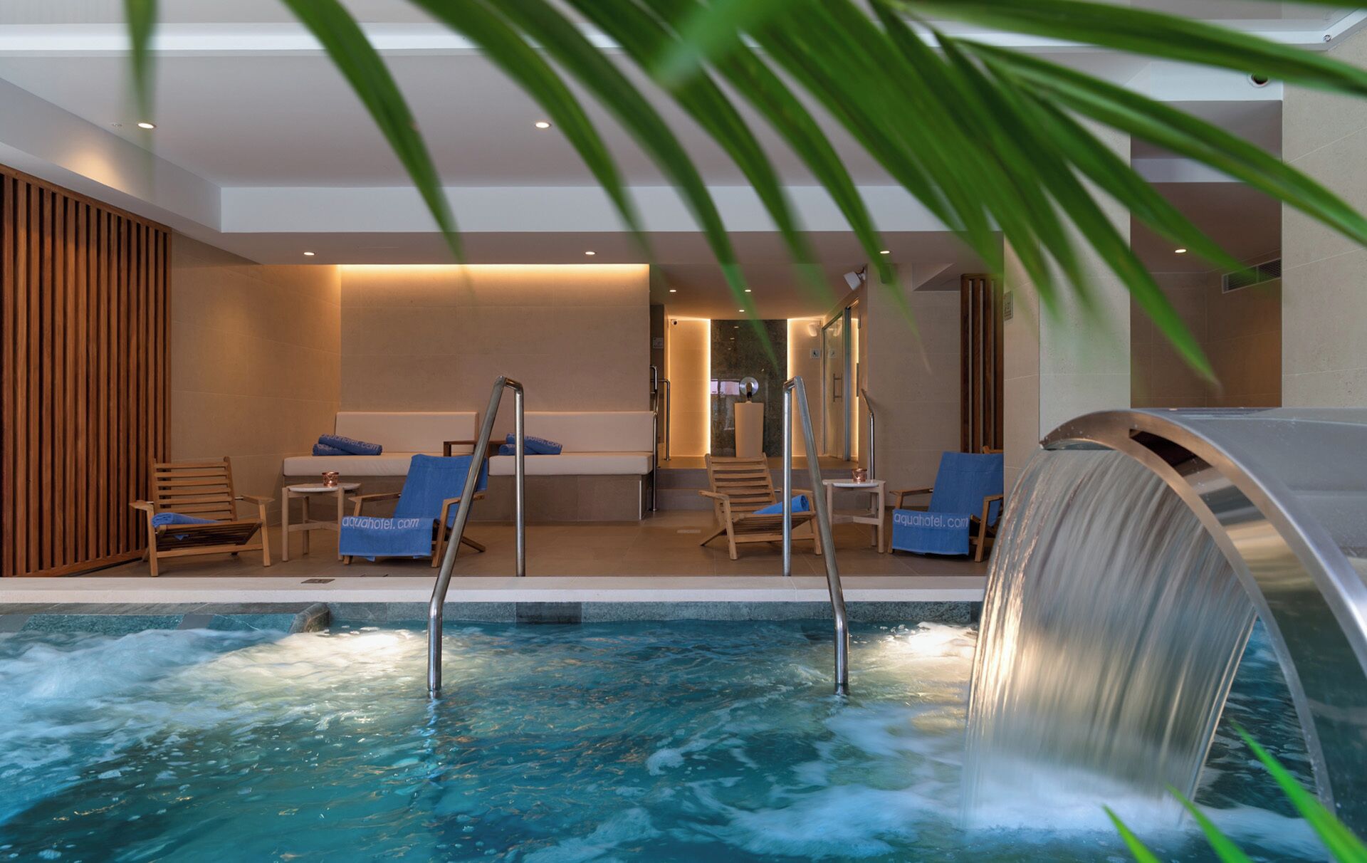 Un espace spa comprenant un bain à remous, des chaises longues et une cascade décorative.
