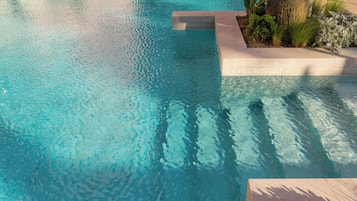 A clear blue pool with a stone edge and surrounding greenery.