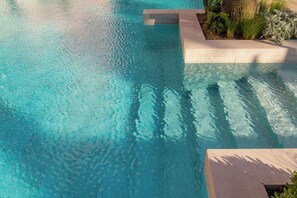 A clear blue pool with a stone edge and surrounding greenery. - AQUA Hotel The Breeze & Spa - All Inclusive - Adults Only +18 (Santa Susanna)