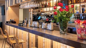 Una zona de bar con una barra alargada, taburetes, una vitrina de vidrio con botellas y un jarrón con flores rojas.