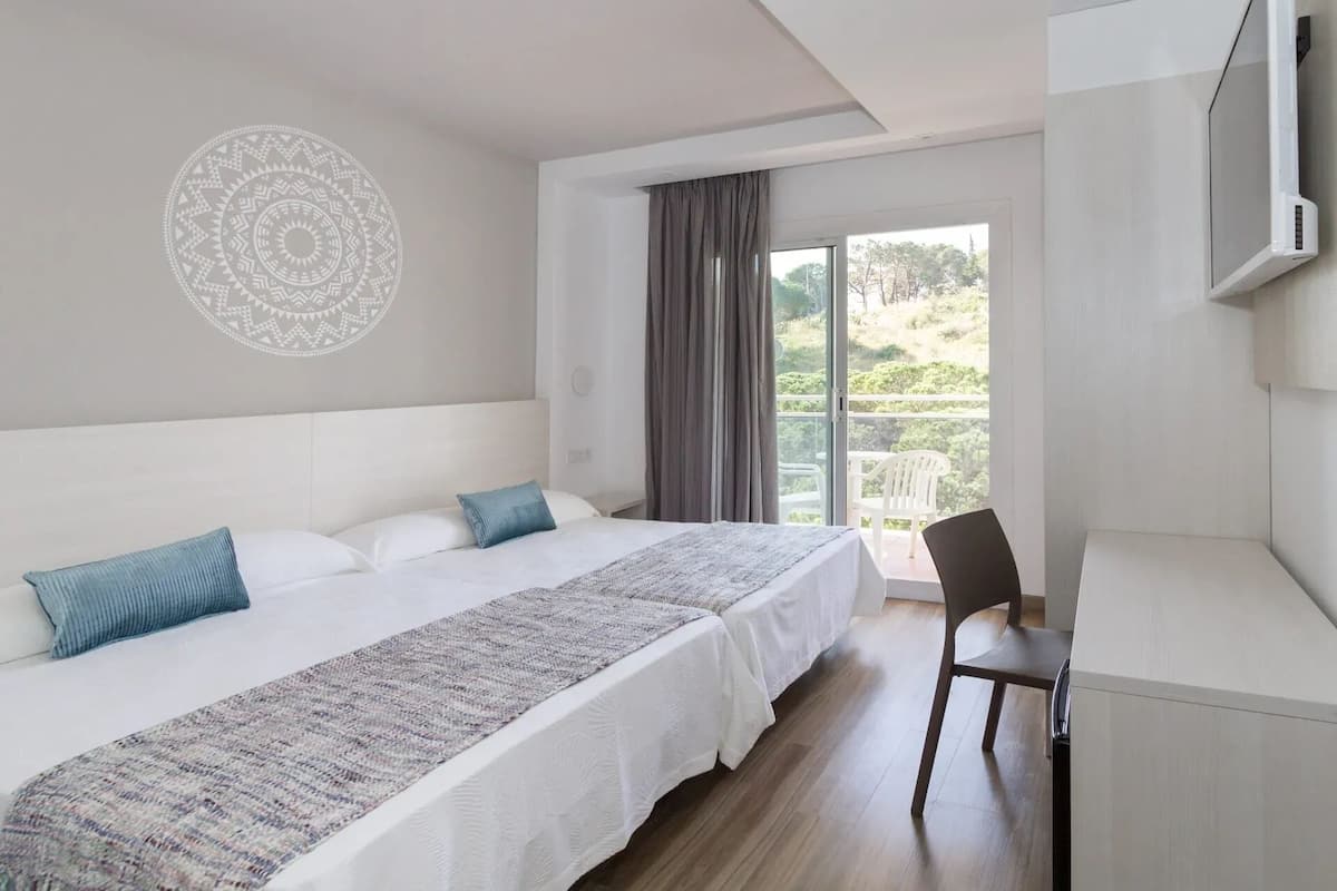 Un dormitorio con cama, escritorio, silla, un ventanal grande y un adorno en la pared.