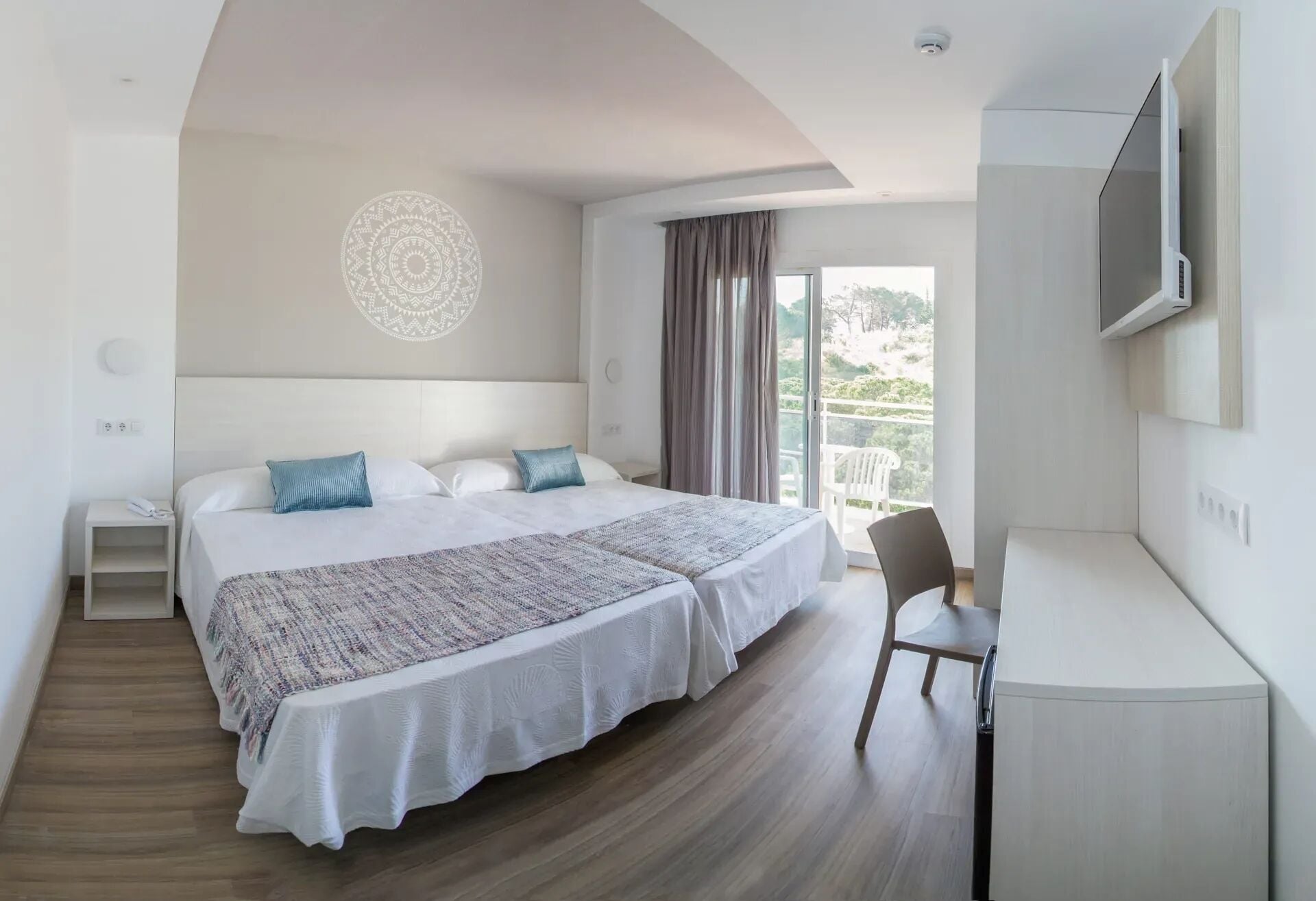 Ein Hotelzimmer mit Bett, Schreibtisch, Stuhl, Fernseher und einem Balkon mit Vorhängen.