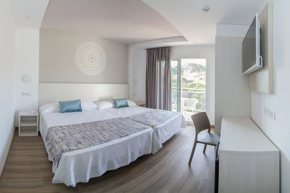 A hotel room with a bed, a desk, a chair, a TV, and a balcony with curtains.