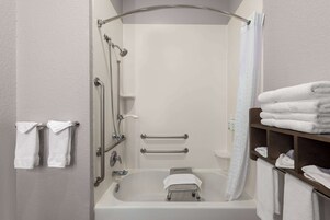 Une salle de bain moderne équipée d’une baignoire, de barres d’appui et d’une étagère avec des serviettes.