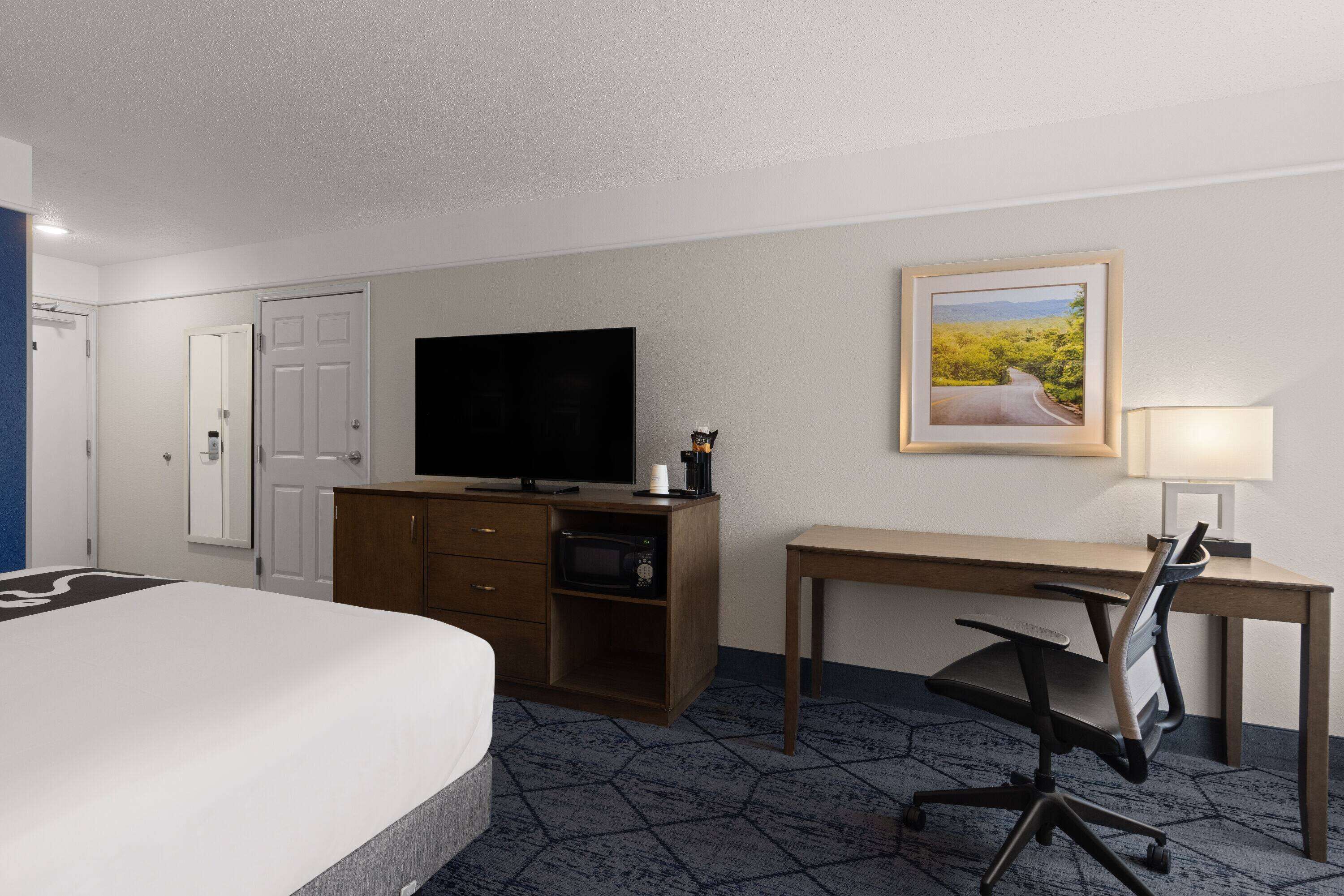A hotel room with a bed, a desk, a television, a desk lamp, and a painting on the wall.