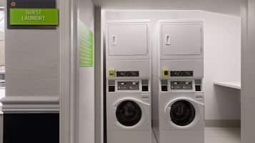 Un espace buanderie à la disposition des clients, équipé de deux machines à laver superposées et d’un panneau indiquant l’emplacement.