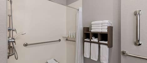 Un baño con ducha, barras de apoyo, un taburete pequeño y un estante con toallas.