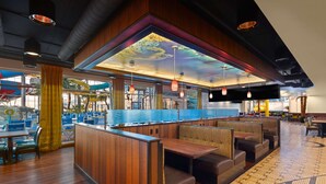 Un restaurante con cabinas de madera, un ventanal grande con vista a una piscina y un techo con un mural colorido.