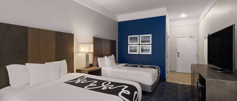 Habitación de hotel con dos camas, televisor, escritorio y una pared decorada en azul.