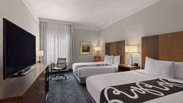 A hotel room with two beds, a TV, a desk, and a chair.
