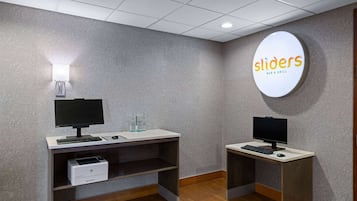 A hotel room with two desks, each with a computer and keyboard, and a printer.