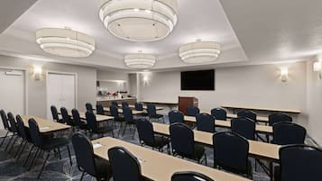A conference room with multiple tables and chairs, a flat-screen TV, and ceiling lights.