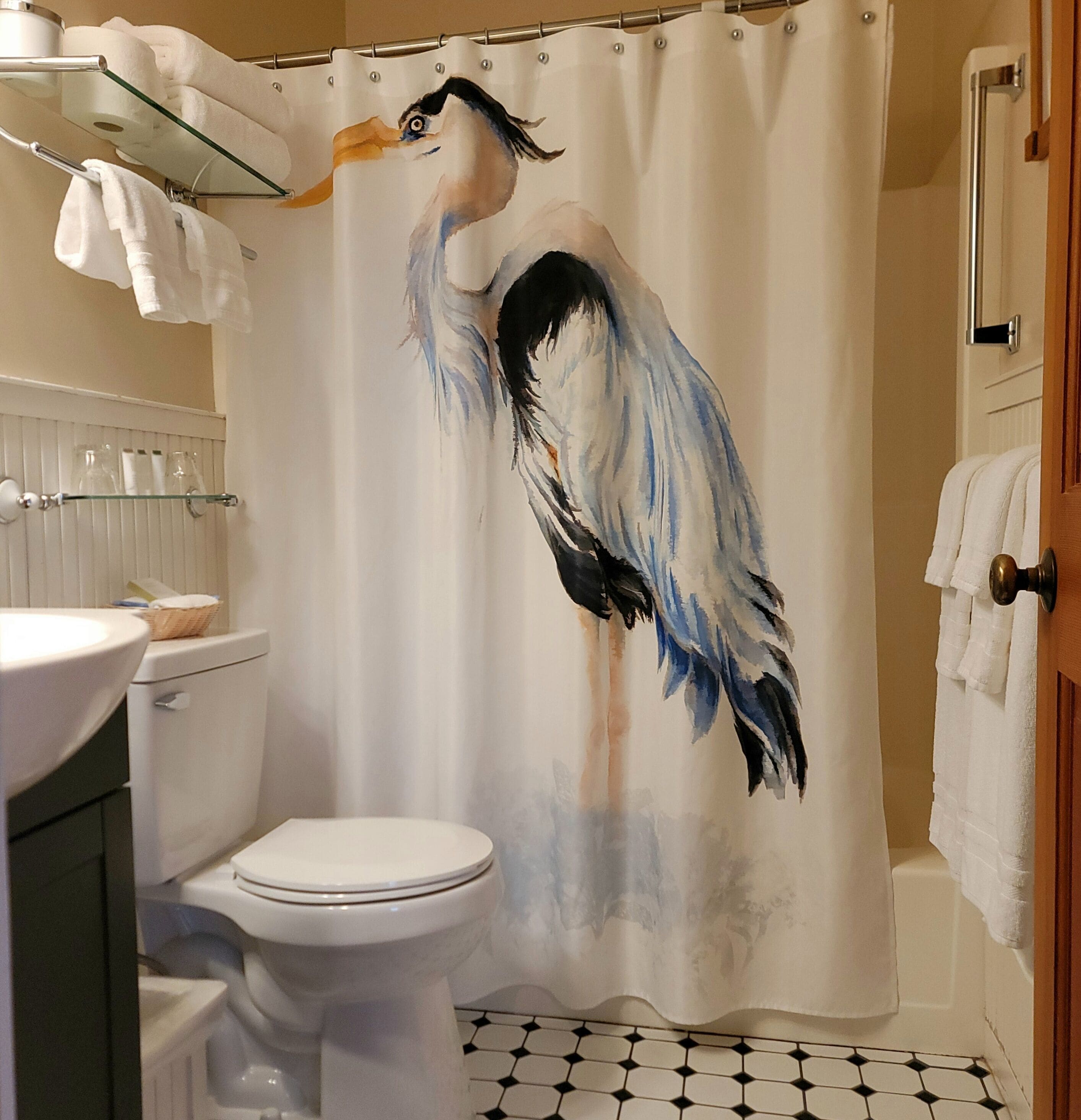 A bathroom with a shower curtain featuring a bird design, a toilet, a sink with a basket, and towels hanging on the wall.