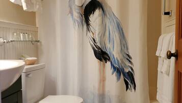 A bathroom with a shower curtain featuring a bird design, a toilet, a sink with a basket, and towels hanging on the wall.