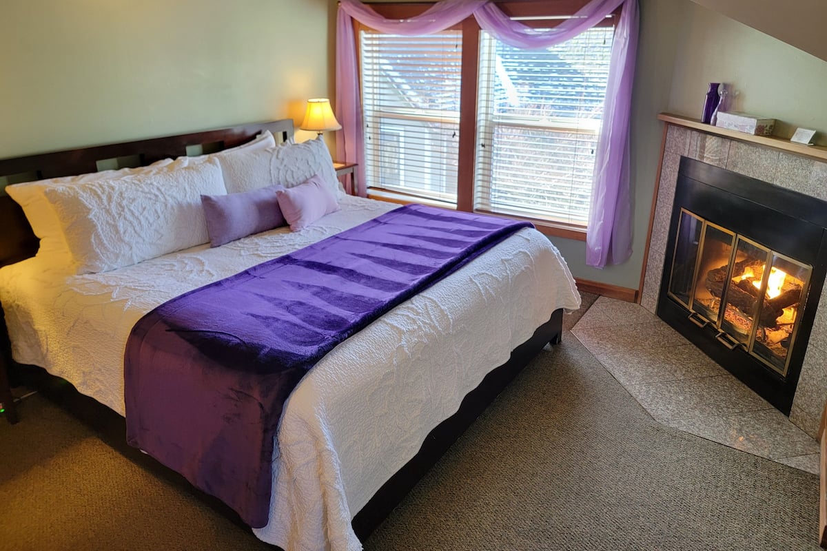 A bedroom with a bed, a fireplace, and a window with blinds.